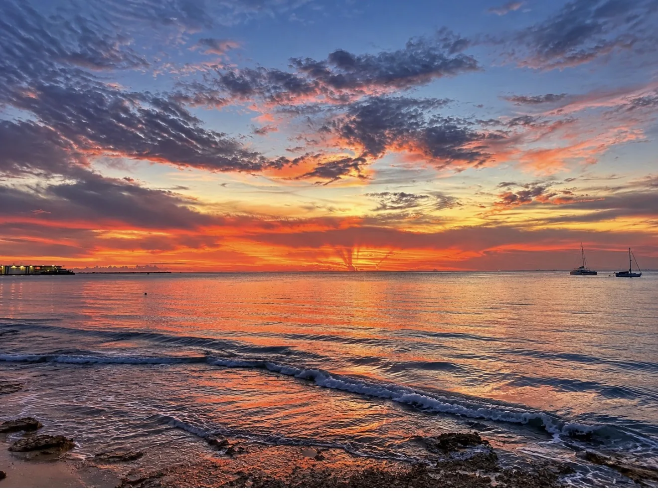 Sailboats anchored off Cozumel under a brilliant orange sunset sky